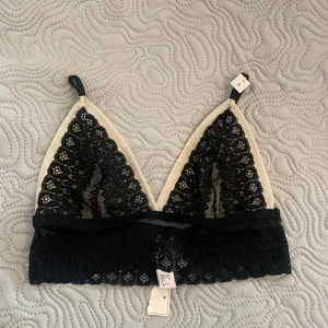 Svart spets bralette - Säljer en elegant svart spets bralette med justerbara axelband. Den har en vacker spetsdesign och en mjuk vit insida. Oanvänd.