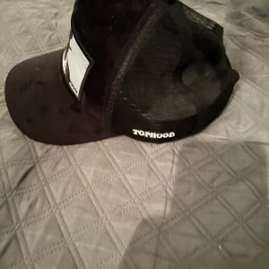 Svart keps med nätpaneler - Snygg svart keps med nätpaneler och ett tryck framtill. Kepsen har justerbar rem baktill för perfekt passform. Den är i ny skick