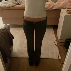 Svarta bootcut jeans - Snygga svarta bootcut jeans som har syts mer lågmidjat och klassisk fickor med knappar. Jeansen har dekorativa knappar på bakfickorna och grå urtvättade 