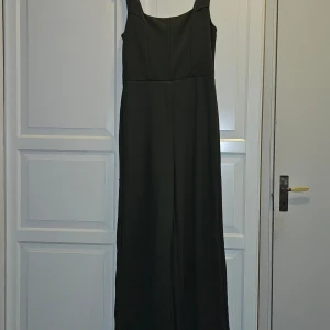 Grön jumpsuit från Amisu - Elegant grön jumpsuit från Amisu med breda axelband och en stilren design. Perfekt för en chic look. Klänningen har en klassisk passform som ger en smickrande siluett.