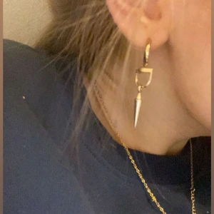 Maria Nilsdotter liknande - Snygga guldörhängen med en unik design. De har en rund ring och en hängande spetsig detalj som ger en edgy look. Perfekta för att ge din outfit en extra touch av stil. Liknar Maria Nilsdotter. Gjort själv. Obs detta är då inte ett Maria Nilsdotter örhänge endast liknande!