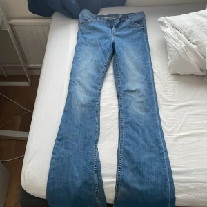 Blå bootcut jeans - Snygga blå bootcut jeans med klassisk femficksdesign och knappgylf. Perfekta för en avslappnad stil. De har en lätt tvättad look som ger en vintage känsla.