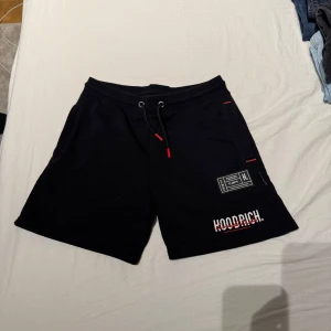 Svarta shorts från Hoodrich - Snygga svarta shorts från Hoodrich med elastisk midja och snörning. De har en cool design med tryckdetaljer i vitt och rött på framsidan. Perfekta för en avslappnad stil. Passar storlek Xs, pris kan diskuteras 