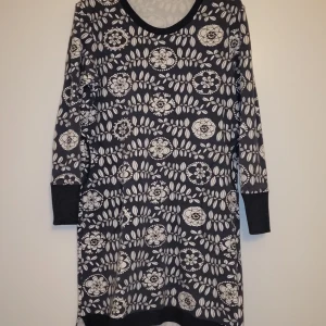 Gråblå och vit mönstrad klänning - Säljer en gråblå klänning med vitt blommönster. Klänningen har långa ärmar och en bekväm passform. Perfekt för en avslappnad stil. Tyg från Paapii. 