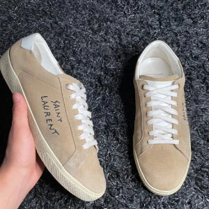 Beige sneakers från Saint Laurent - Snygga beige sneakers från Saint Laurent med vit snörning och vit häl. Skorna har en stilren design med Saint Laurent-logga på sidan och baksidan. Perfekta för en avslappnad och trendig look.