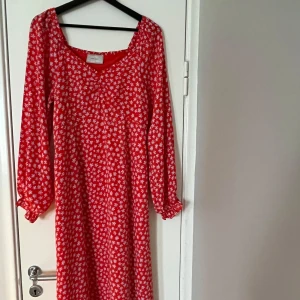 Röd blommig klänning från Neo Noir - Charmig röd klänning från Neo Noir med ett vitt blommönster. Klänningen har långa ärmar och en bekväm passform. Perfekt för en somrig look med sin livfulla färg och mönster.