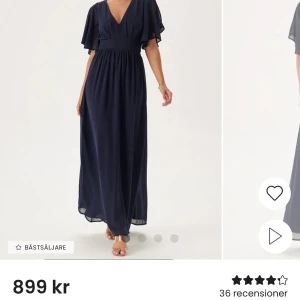 Mörkblå balklänning klänning med v-ringning - Elegant mörkblå balklänning med v-ringning och kortärmade volangärmar. Klänningen har en knytning i midjan och en liten öppning i ryggen. Perfekt för en stilfull kväll.