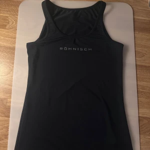 Träningslinne från Röhnisch - Snygg och funktionell svart linnetopp från Röhnisch. Perfekt för träning med sin bekväma passform och stilrena design. Toppen har en rund halsringning och ärmlös stil. 