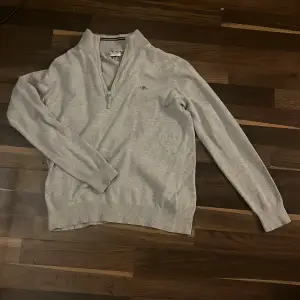 Säljer en stilren grå tröja från Gant med halv dragkedja och broderad logga på bröstet. Tröjan har långa ärmar och ribbade muddar vid ärmslut och nederkant. Perfekt för en avslappnad look. (Pris kan diskuteras)