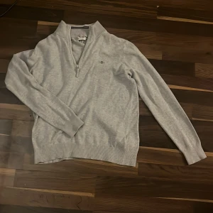 Grå tröja med dragkedja - Säljer en stilren grå tröja från Gant med halv dragkedja och broderad logga på bröstet. Tröjan har långa ärmar och ribbade muddar vid ärmslut och nederkant. Perfekt för en avslappnad look. (Pris kan diskuteras)
