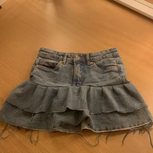 Jeanskjol med volang från LAB Industries - Snygg jeanskjol från LAB Industries med volangdetaljer. Kjolen har en klassisk blå denimfärg och är tillverkad av hållbart material. Perfekt för en trendig look!