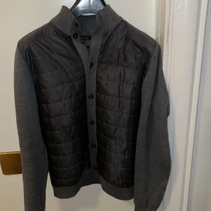 Grå cardigan från Massimo Dutti - Snygg grå cardigan från Massimo Dutti med quiltad framsida och stickade ärmar. Jackan har knappar framtill och en stilren design som passar perfekt för höst och vår. Den är långärmad och har en bekväm passform.