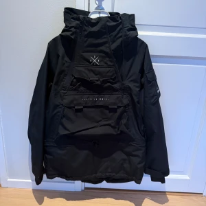 Svart skidjacka från Dope - Säljer en svart vindjacka från Dope med en stor ficka framtill och justerbar huva. Jackan har en stilren design med dragkedja och kardborreband vid ärmsluten. Perfekt i skidbacken. https://www.dopesnow.com/se/akin-w-skidjacka-kvinna-black