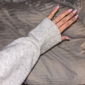 Grå stickad tröja med v-ringning - Grå stickad tröja med v-ringning och långa ärmar. Tröjan har en ribbad kant vid ärmslut och nederkant.