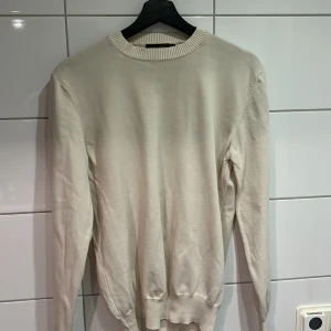 Oscar Jacobson tröja - Säljer en stilren beige tröja från Oscar Jacobson, tillverkad i Italien. Tröjan har en klassisk rund hals och långa ärmar, perfekt för en elegant och avslappnad look. Tröjan är helt ny och enbart testad, skriv vid funderingar!