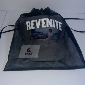 Grå keps från Revenite - Snygg grå keps från Revenite med ett coolt tryck av en bil och en person på framsidan. Kepsen har ett nätmaterial på sidorna och baksidan för extra ventilation. HAR BARA EN SÅ VA SNABBA