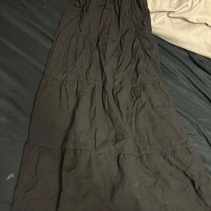 Svart långkjol från H&M - Snygg svart långkjol från H&M med elastisk midja. Perfekt för en stilren look. Kjolen har en enkel design som gör den lätt att matcha med olika toppar.