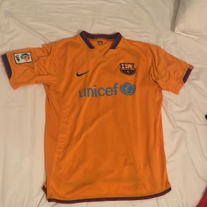 Orange Barcelona tröja - Säljer en orange fotbollströja Barcelona från Nike. Tröjan har ett broderat klubbmärke på bröstet och Unicef-logga i blått. Detaljer i rött och blått vid krage och ärmslut. Mycket gott skick!