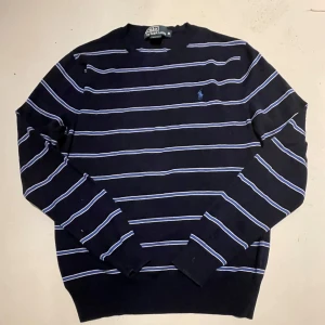 Mörkblå randig tröja från Ralph Lauren - Säljer en stilren mörkblå tröja från Ralph Lauren med vita ränder och broderad logga på bröstet. Tröjan har en slim fit passform och långa ärmar, perfekt för en klassisk look. Jätte bra skick och kan diskutera priset