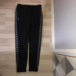 Svarta träningsbyxor från Kappa - Träningsbyxor från Kappa med det klassiska logotypmönstret längs sidorna. Byxorna har en elastisk midja och är och benslut. Dom är använda och lagade i grenen (bild 4)