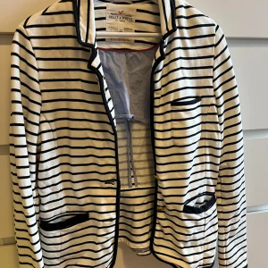 Randig kavaj från Holly & White - Snygg randig kavaj från Holly & White i svart och vit. Den har långa ärmar och dekorativa knappar i guld. 