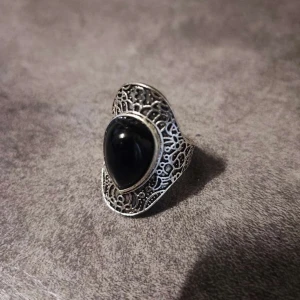 Silverring med svart sten - Elegant silverring med en stor svart sten i centrum. Ringen har ett detaljerat filigranmönster som ger en vintagekänsla. Perfekt för att ge en stilfull touch till din outfit.