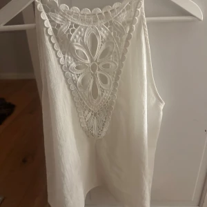 Superfint linne - Säljer en stilren vit ärmlös topp med vacker spetsdetalj framtill. Perfekt för varma dagar eller som ett lager under en kavaj. Toppen har en luftig passform och är gjord i ett mjukt material. Den är från zara, superfin verkligen!