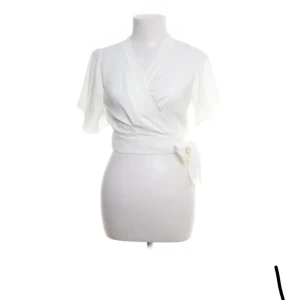 Vit omlottblus - Säljer en stilren vit omlottblus med korta ärmar och knytning i midjan. Perfekt för en elegant och avslappnad look.