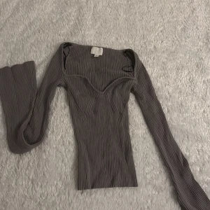 Grå ribbad topp - Snygg grå ribbad topp med långärmad design och en v-ringad stil. Perfekt för en stilren look.