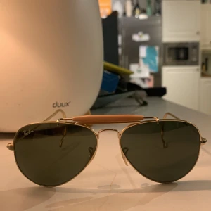 Aviator solglasögon från Ray-Ban - Klassiska aviator solglasögon från Ray-Ban med guldfärgad metallram och gröna linser. De har en tunn båge och justerbara nässadlar för extra komfort. Perfekta för en stilren look,           ny pris 1990  De är inga repor och näst intill helt nytt skick finns inga defekter 
