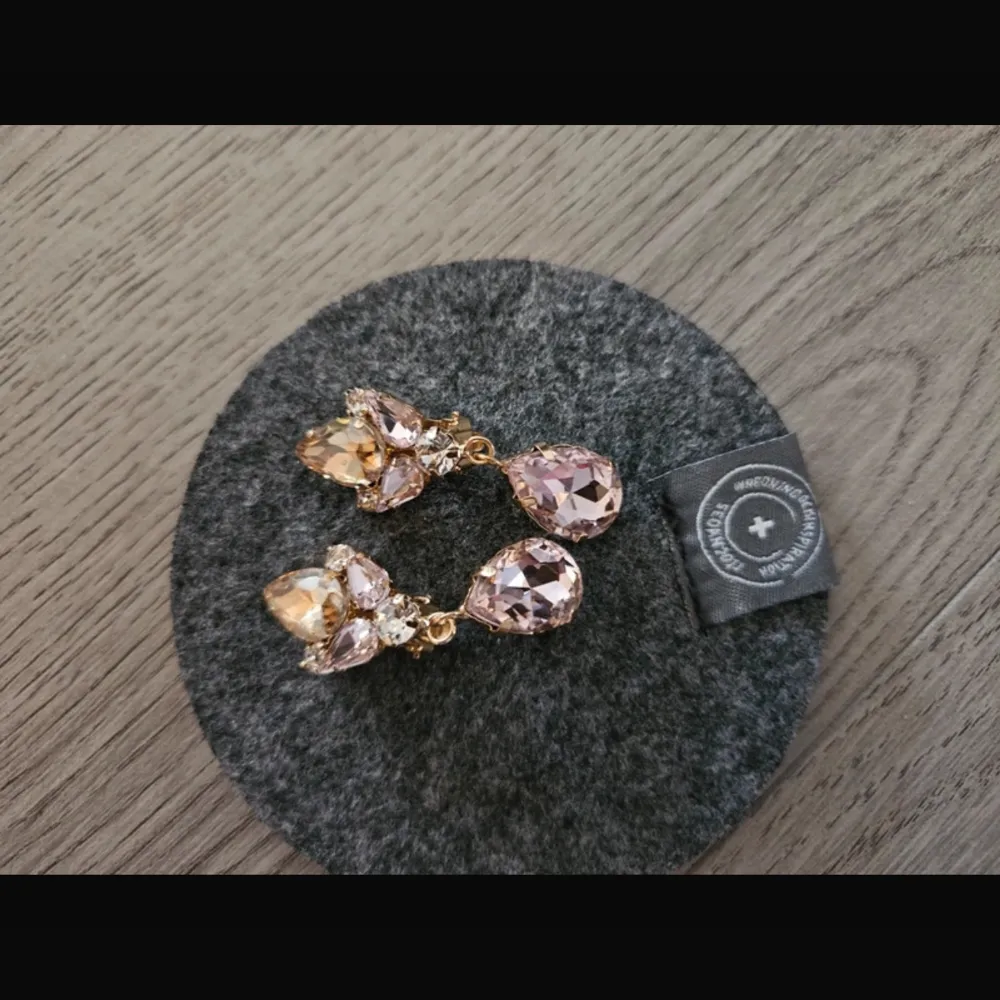 Eleganta örhängen med stora droppformade rosa stenar och mindre klara stenar i en guldinfattning. Perfekta för att ge en glamorös touch till din look. Endast testade. Fick i present (box medföljer). Asusteet.