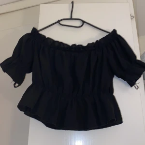 Svart offshoulder topp från Shein - Säljer en svart offshoulder topp från Shein i storlek S. Toppen har korta ärmar och en volangdetalj vid nederkanten, perfekt för en trendig look.