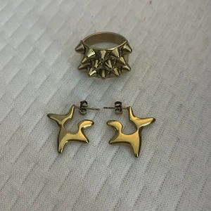 Edblad smycken  - Snyggt smyckeset i guldfärg som inkluderar en unik ring med spetsiga detaljer och matchande örhängen i abstrakt form. Perfekt för att ge en edgy touch till din stil. Ringen har blivit lite silvrig på bak sidan som man ser på bilden men inget som märks. 