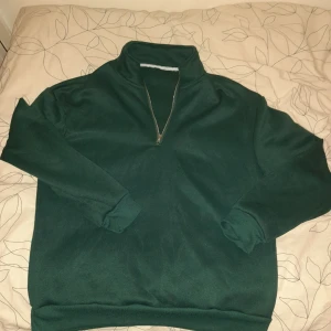 Grön tröja med dragkedja - Säljer en grön tröja med halv dragkedja och hög krage. Tröjan har långa ärmar och är perfekt för kyligare dagar. Den är stilren och enkel att matcha med olika outfits. 