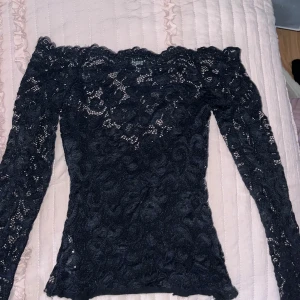 Svart spetsblus från NLY One - Säljer en elegant svart spetsblus från NLY One i storlek XS. Blusen har en offshoulder-design med långa ärmar och ett vackert spetsmönster. Perfekt för en stilfull look.