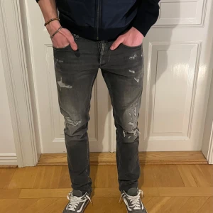 Replay Grover Jeans - Gråa Replay hyperflex jeans med slitningar i storleken W30/L34. Jeansen är sydda till att sitta som längd 32, de ser helt vanliga ut trots att de är sydda nere i sömmarna!