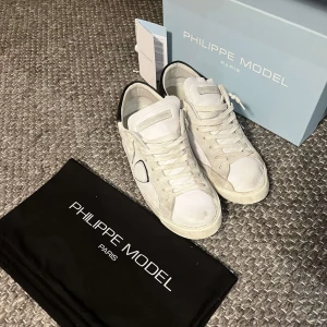 Philippe Model skor - Snygga vita sneakers från Philippe Model med svarta detaljer på hälen. Köpta för 2-3 månader sen, fortfarande i väldigt bra skick. Storlek 43 bara höra av sig vid frågor och funderingar. 