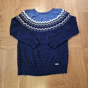 Mönstrad stickad tröja från Collection L - Säljer en snygg stickad tröja från Collection L i blått med ett stilrent mönster runt halsen. Tröjan har långa ärmar och ribbstickade muddar. Perfekt för kyligare dagar! Sparsamt använd. Storlek L men passar som en small. Axelbredd 47  Längd 62