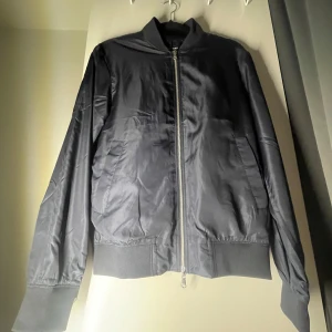 Svart bomberjacka från J.Lindeberg - Snygg svart bomberjacka från J.Lindeberg med dragkedja framtill. Jackan har en klassisk design med ribbade muddar vid ärmslut och nederkant. Perfekt för en stilren look.