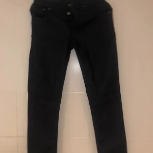 Nudie jeans - Snygga mörkblå jeansbyxor med knappar framtill. De har en klassisk design och passar perfekt för en stilren look. Perfekta för både vardag och mer uppklädda tillfällen.