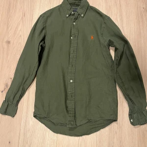 Grön skjorta från Polo Ralph Lauren - En mörkgrön Ralph Lauren skjorta med orange tryck, storlek XS (Amerikanst mått), passar som S. Fräsch skjorta, bra inför varmare dagar. Inga fel på skjortan.