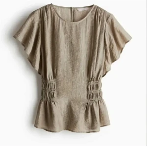 Beige blus med rynkdetaljer - Snygg beige blus med korta ärmar och rynkdetaljer i midjan. Perfekt för en stilren look. Tillverkad i ett lätt och luftigt material.