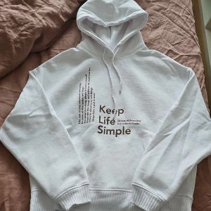 Vit hoodie från Amisu - Säljer en vit hoodie från Amisu med texten 'Keep Life Simple' tryckt på framsidan. Den har en klassisk design med huva och dragsko samt ribbade muddar vid ärmslut och nederkant. Perfekt för en avslappnad stil.