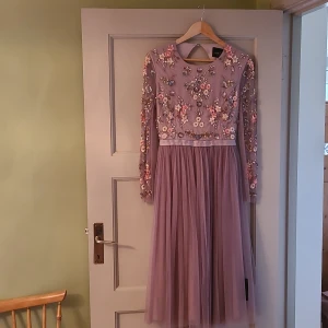 Needle and thread fantastisk lila paljettklänning - Elegant lila klänning med långa ärmar och vackra blommiga broderier och paljetter på överdelen. Kjolen är i ett lätt och flödande material som ger en romantisk känsla. Perfekt för speciella tillfällen. Defekter: Små hål närmast dragkedjan där bak och några lösa trådar på vänster arm. 