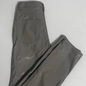 Grå byxor i syntetmaterial - Snygga grå byxor i syntetmaterial med en modern look. De har en rak passform och en midwaist design. Perfekta för en stilren och minimalistisk outfit.