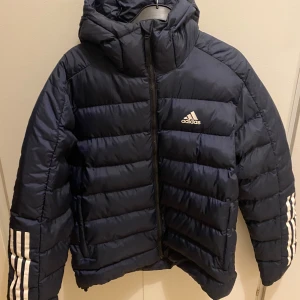 Pufferjacka Adidas herr S marinblå - Nyskick, bara använd ett fåtal gånger. Vadderad, varm o skön. Stl S herr, skulle säga normal i stl. Marinblå.