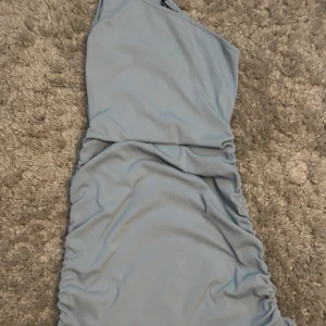 Ljusblå oneshoulder klänning - Säljer en superfin ljusblå oneshoulder klänning i ribbat material. Den är tight och har snygga rynkade detaljer på sidorna som ger en cool look💙
