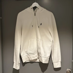 Ralph Lauren hoodie vit - Säljer en vit hoodie från Ralph Lauren i bra skick. Den har en dragkedja framtill och en liten broderad logga bröstet. Storleken är normal och den är superbekväm att ha på sig.