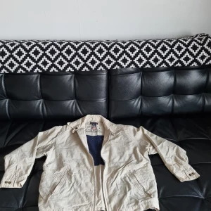 Barn / kids Medium Beige vindjacka från GANT - Säljer en beige barn vindjacka från GANT i bra skick. Jackan har dragkedja och är långärmad med en cool blå meshfoder inuti. Perfekt för vår och höst när det blåser lite extra. Passar både till vardags och lite mer sportiga aktiviteter.