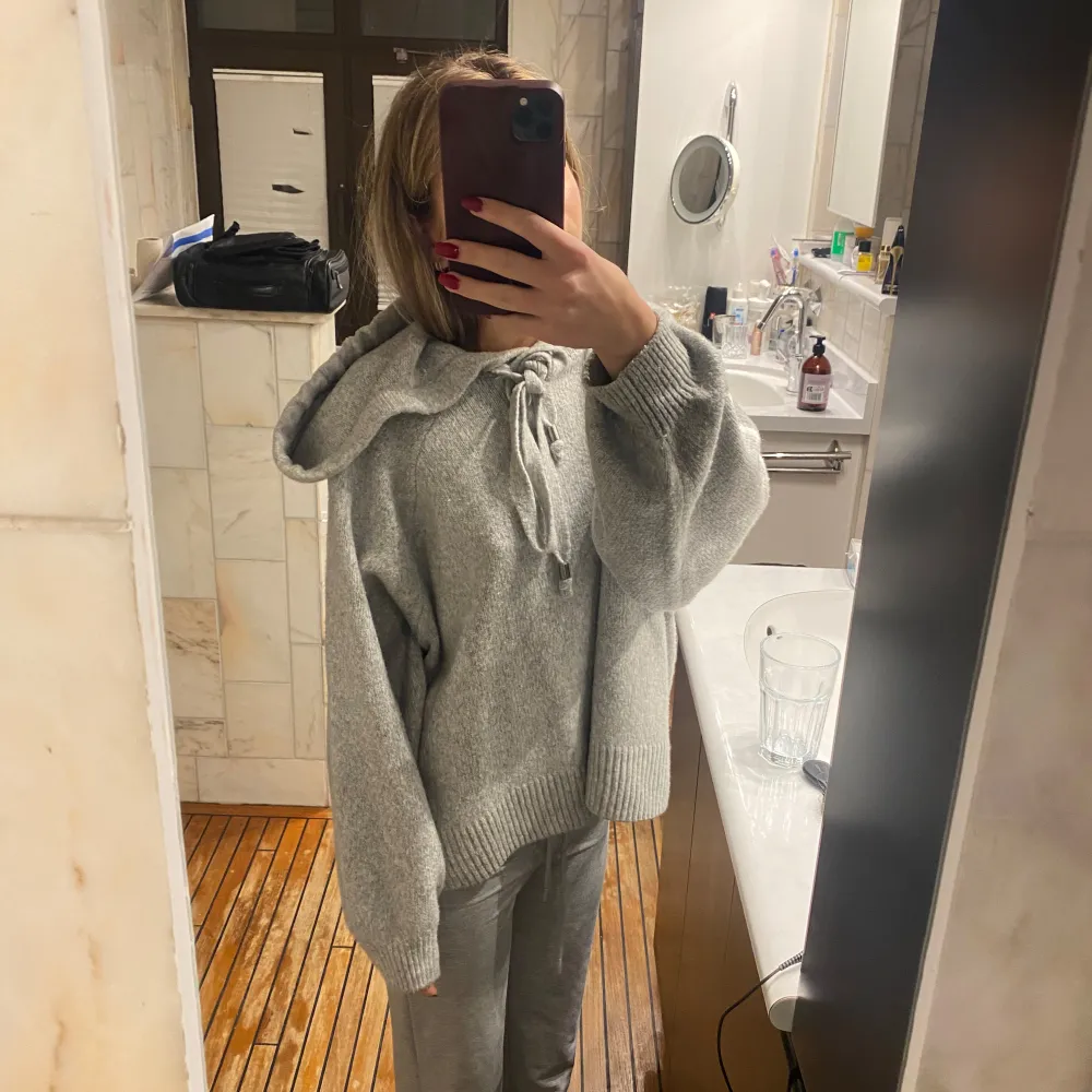 Mysig grå stickad hoodie med en stor luva och knytband framtill. Perfekt för kyliga dagar när du vill vara både bekväm och stilren. Den har en loose passform och långa ärmar med ribbade muddar. Enkelt att matcha med jeans eller mjukisbyxor för en avslappnad look.. Tröjor & Koftor.